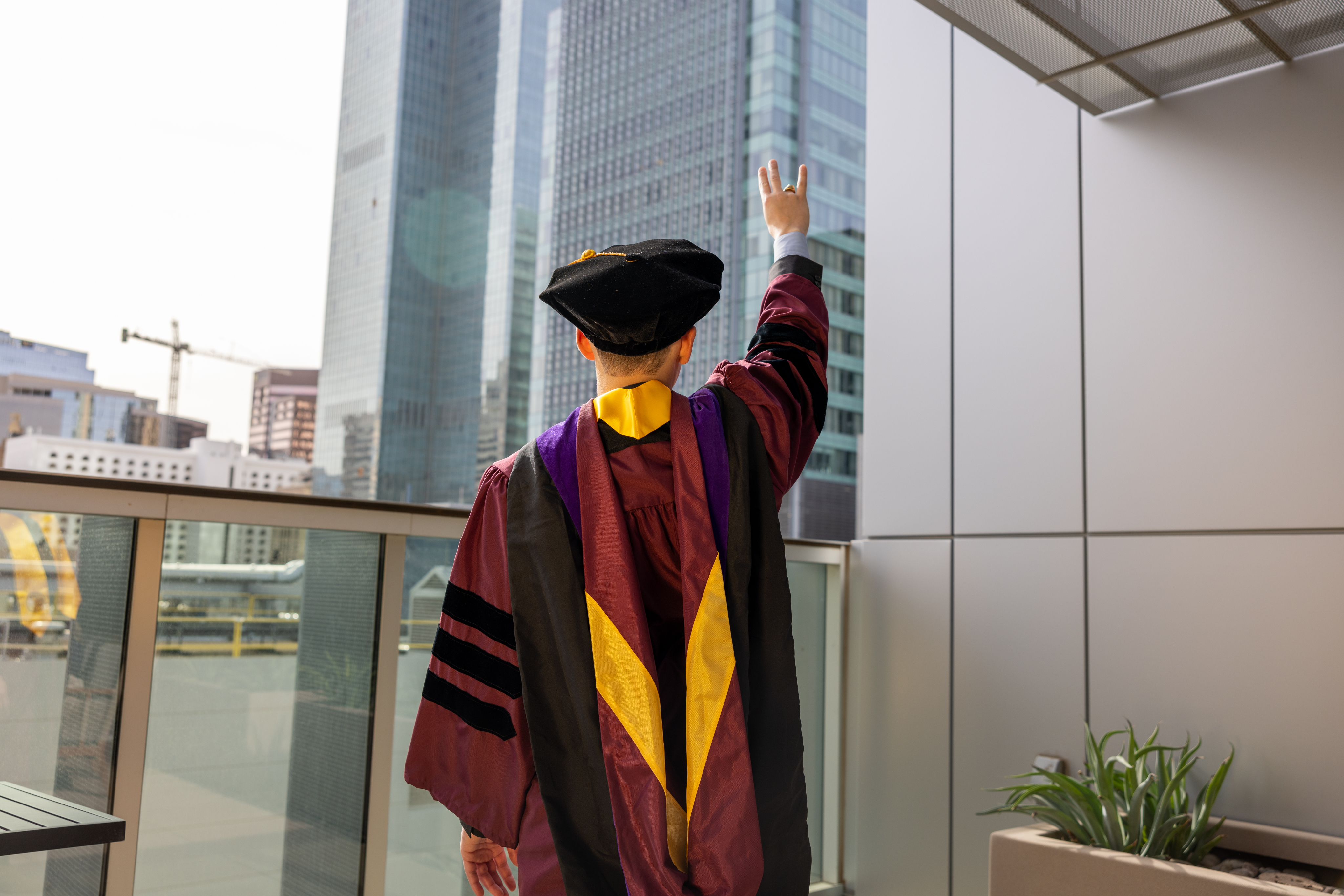 Man in graduation cap and gown holding up hand making the fork symbol